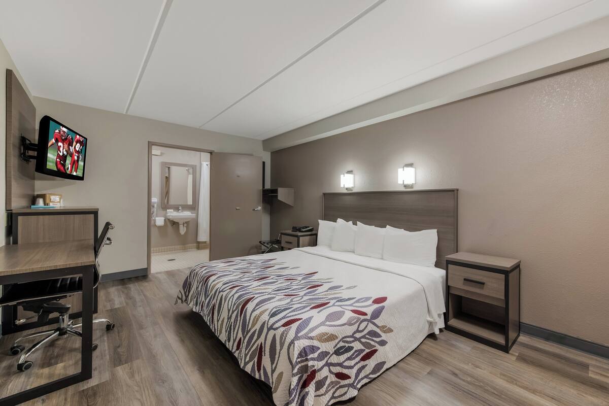 A hotel room with a bed, bedside table, nightstand, desk, chair, and a television on the wall.