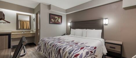 Una habitación de hotel con una cama, mesitas de noche, un espejo y un perchero para toallas.