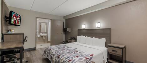 Una habitación de hotel con cama, mesita de noche, escritorio con silla y televisor montado en la pared.