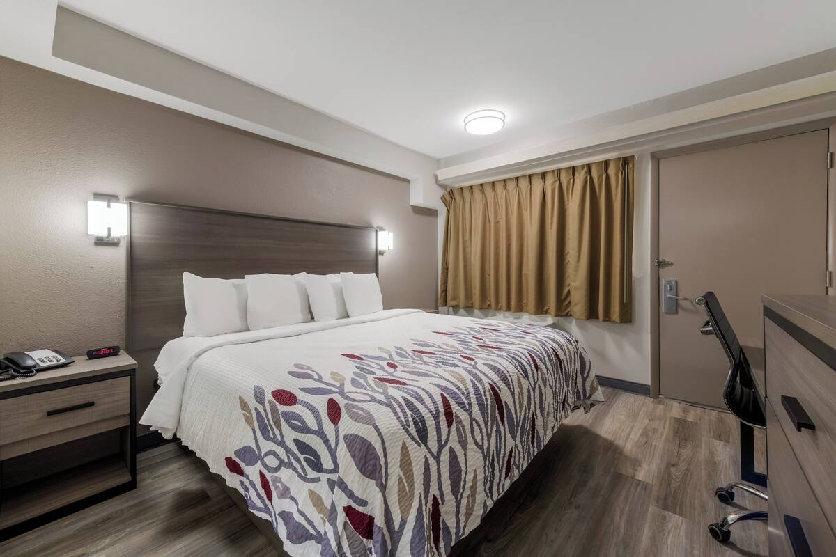 A hotel room with a bed, bedside table, lamp, and a door.