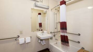 Un baño con un lavabo blanco, un espejo, una ducha con cortina a rayas rojas y blancas, y un tapete de baño de madera.