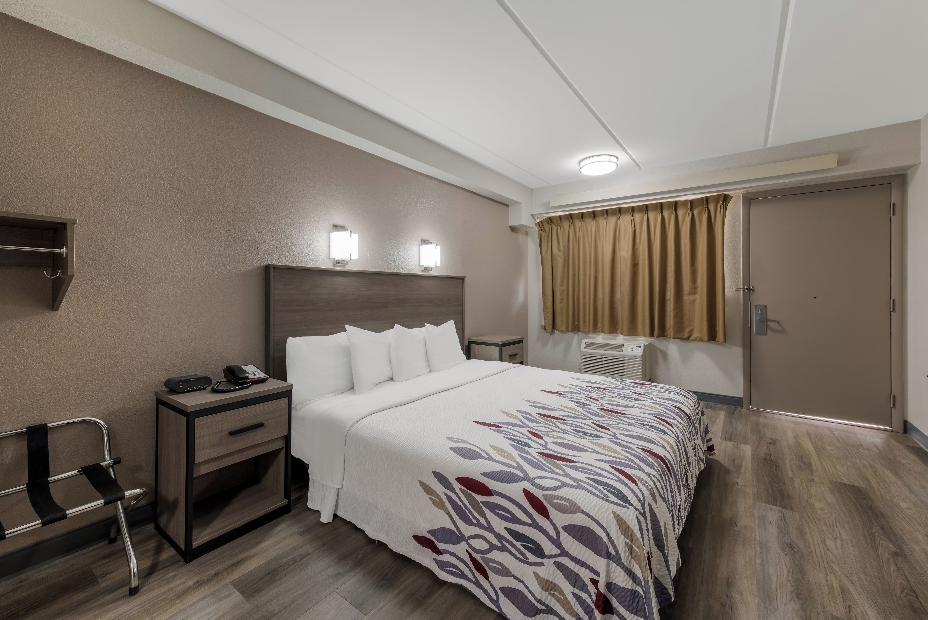 A hotel room with a bed, bedside table, lamp, and a window with curtains.