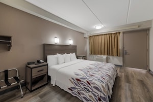 Una habitación de hotel con cama, mesita de noche, lámpara y ventana con cortinas.