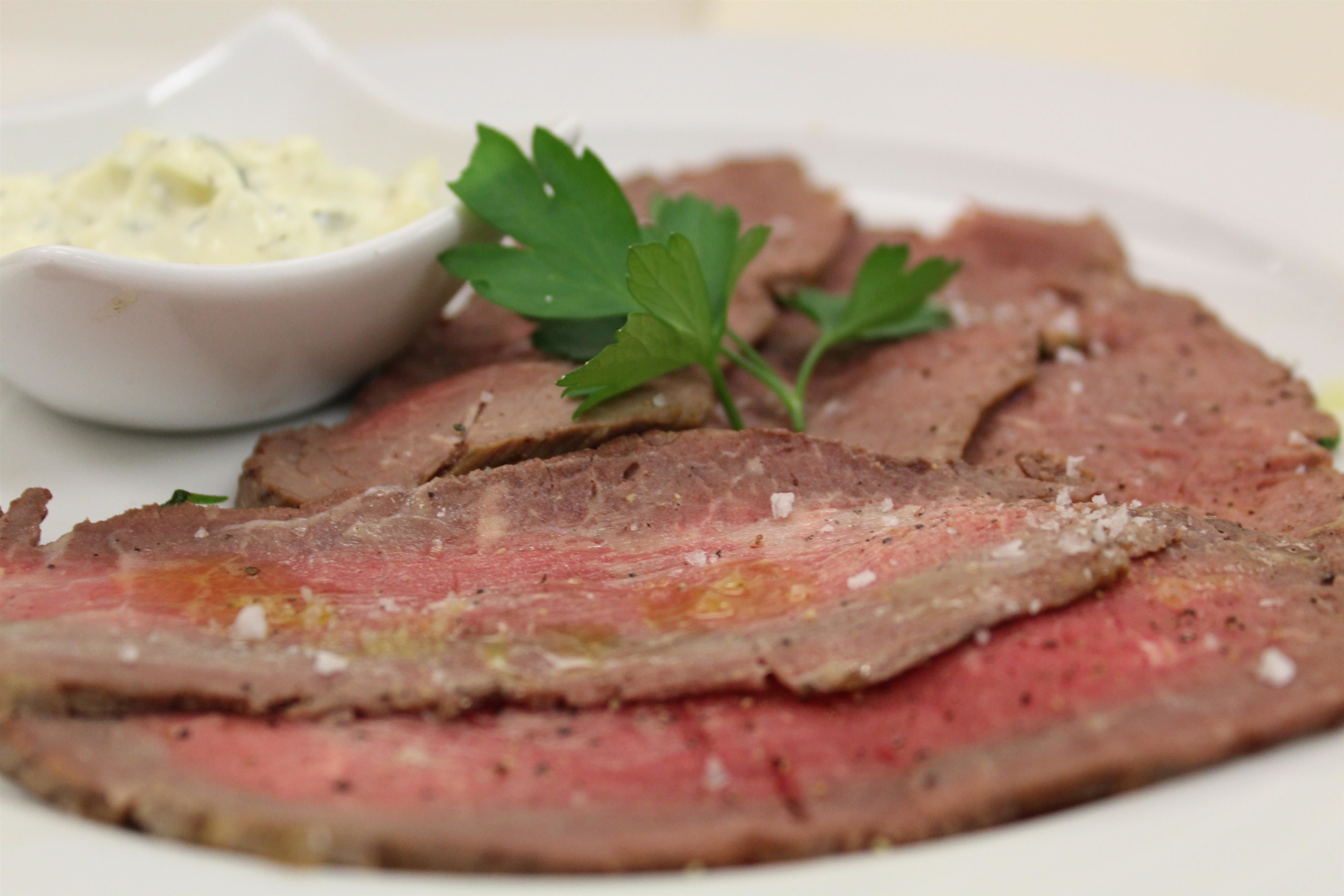 A plate of sliced beef with a side of creamy sauce and parsley garnish.