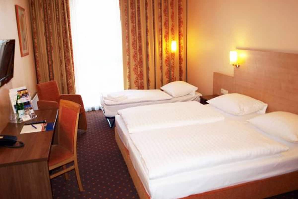 A hotel room with two beds, a desk, a chair, and a television on the wall.