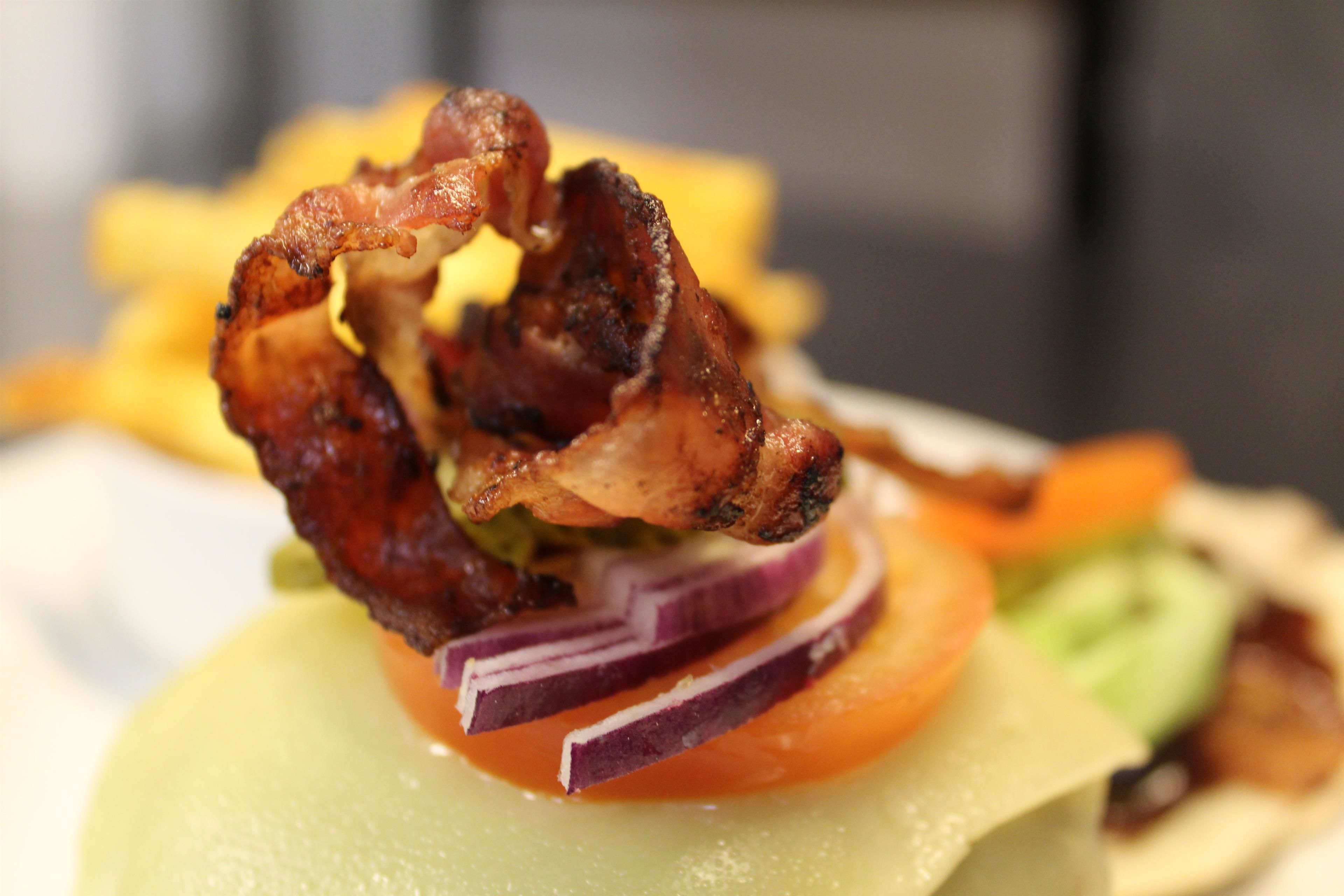 A close-up of a food item with crispy bacon on top, surrounded by sliced vegetables.