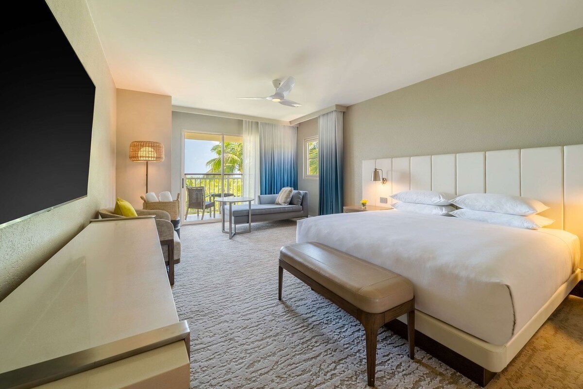 Une chambre d’hôtel avec un grand lit, un bureau, une chaise, un canapé et un balcon avec des rideaux.