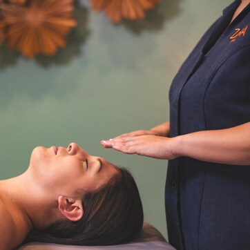 A person lying down with a hand on their forehead, possibly receiving a massage, in a room with a green wall and a decorative item above.