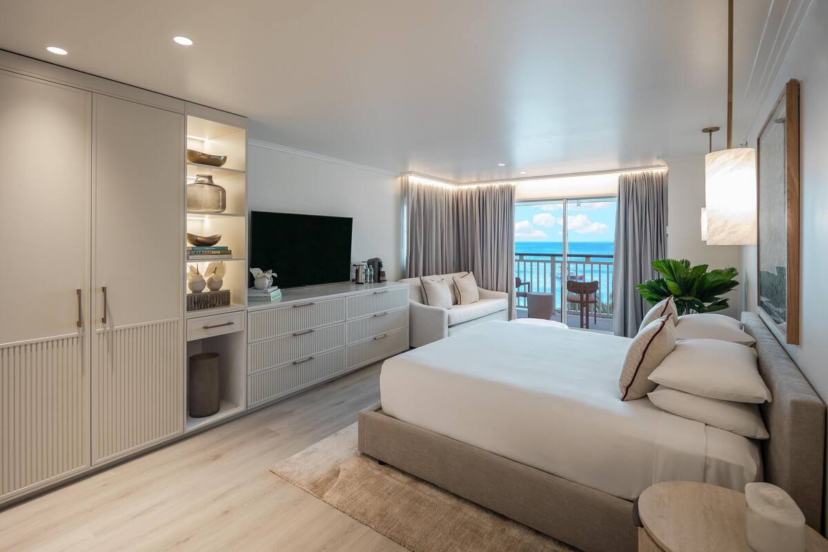 A modern bedroom with a large bed, a TV, a balcony with curtains, and a storage unit with shelves.