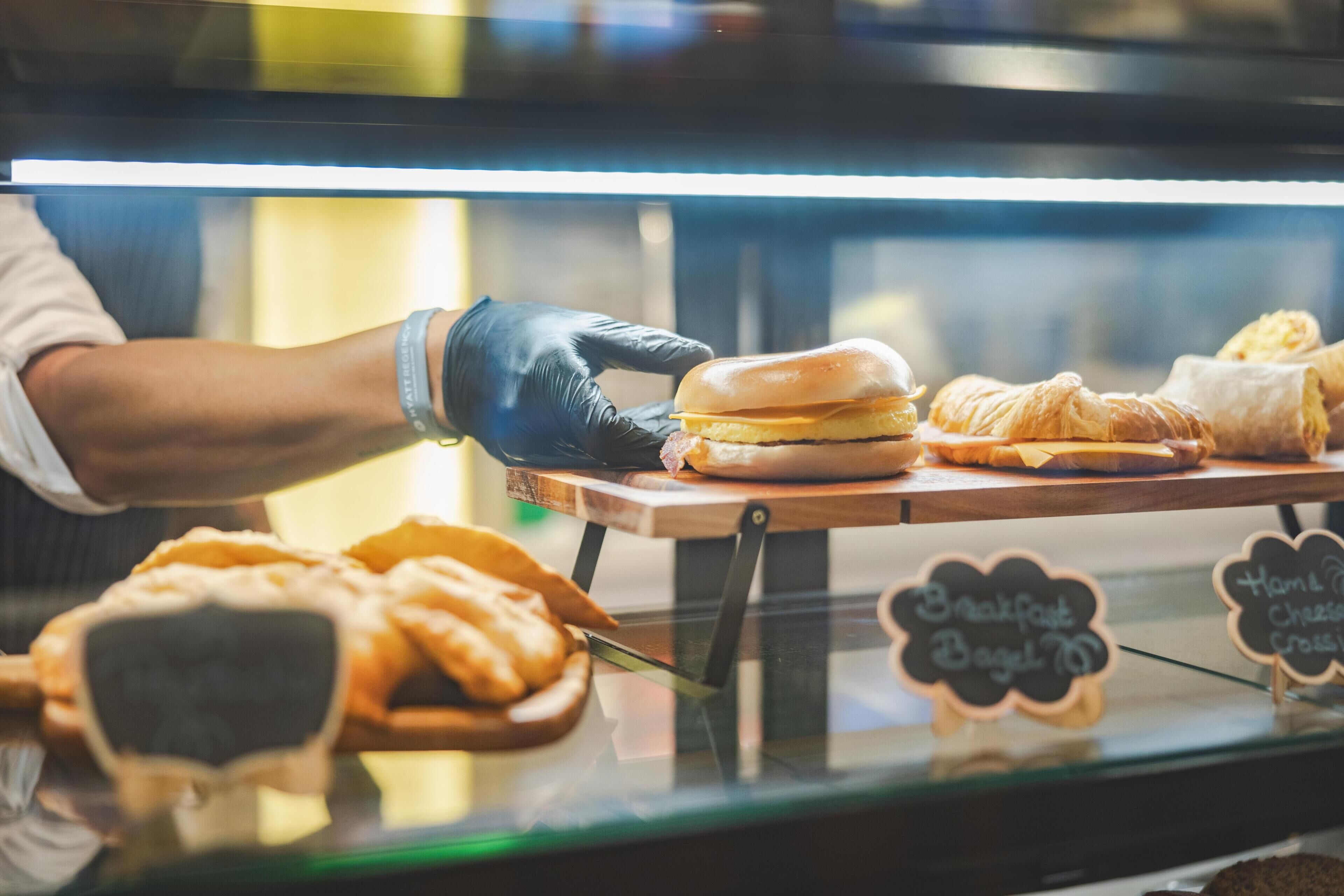 A bakery display with a sandwich, croissants, and a sign indicating 'Breakfast Bagel.'