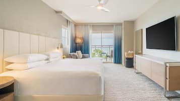 Une chambre d’hôtel équipée d’un lit, d’une télévision, d’un bureau, d’un ventilateur de plafond et d’un balcon avec des rideaux.