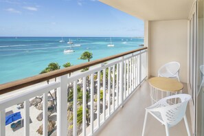 Un balcon avec vue sur l’océan, des chaises blanches et une table.