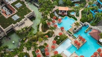 Vista aérea de un complejo turístico con varias piscinas, palmeras y senderos de piedra.