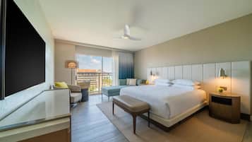 Ein modernes Hotelzimmer mit einem großen Bett, einem Schreibtisch, einem Sessel, einer Bank, einem Nachttisch mit Lampe und einem Deckenventilator.