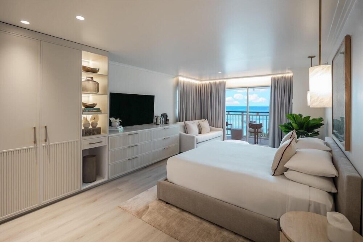 Une chambre moderne avec un grand lit, une télévision, un balcon avec des rideaux et un meuble de rangement avec des étagères.