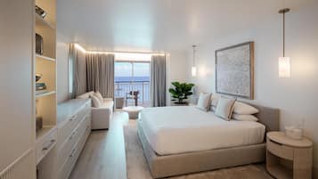 Una camera d'hotel moderna con un letto grande, un angolo salotto, vista sul mare e un armadio a muro.