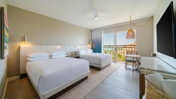 Habitación de hotel con dos camas, un balcón con mesa y sillas, ventilador de techo y televisor en la pared.