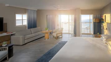 Habitación de hotel con cama, sofá, una mesita con planta, televisor y balcón con vistas.
