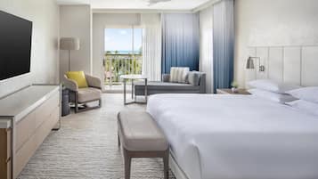 Habitación de hotel con cama, escritorio, silla, banco, televisor y vistas al exterior.