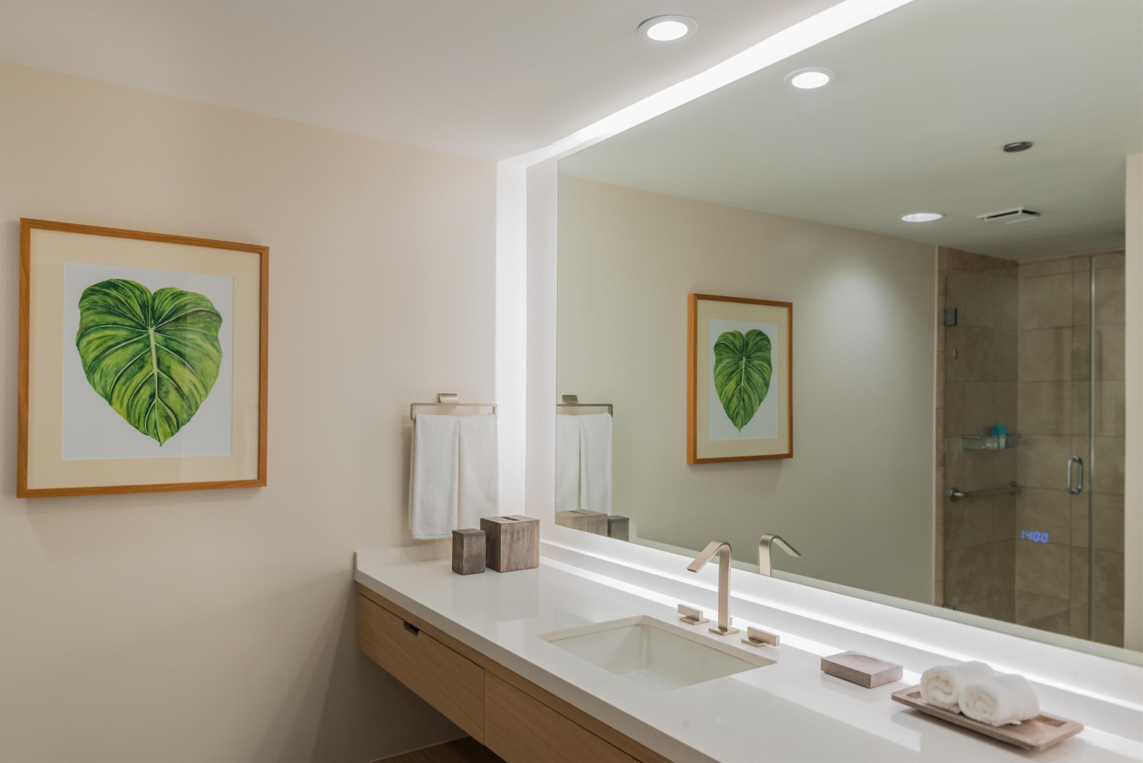 Un baño moderno con un espejo grande, un lavamanos y una ducha.