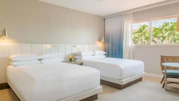 Een hotelkamer met twee bedden, een plafondventilator, een raam met uitzicht op palmbomen, en een klein tafeltje met een stoel.