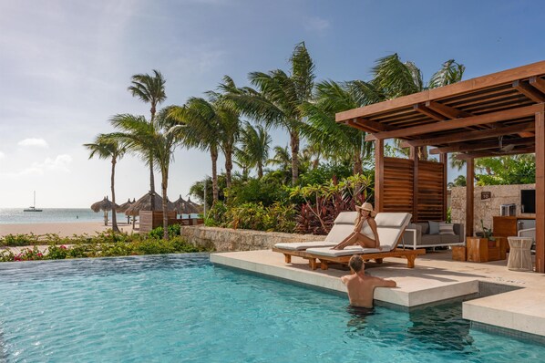 Un espace aménagé au bord de la piscine, avec des chaises longues, une pergola en bois et une vue sur la plage.