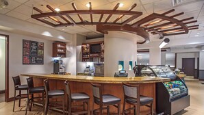 A bar area with a curved counter, bar stools, a coffee machine, and a refrigerated display. - Hyatt Place Cincinnati/Blue Ash (Cincinnati)