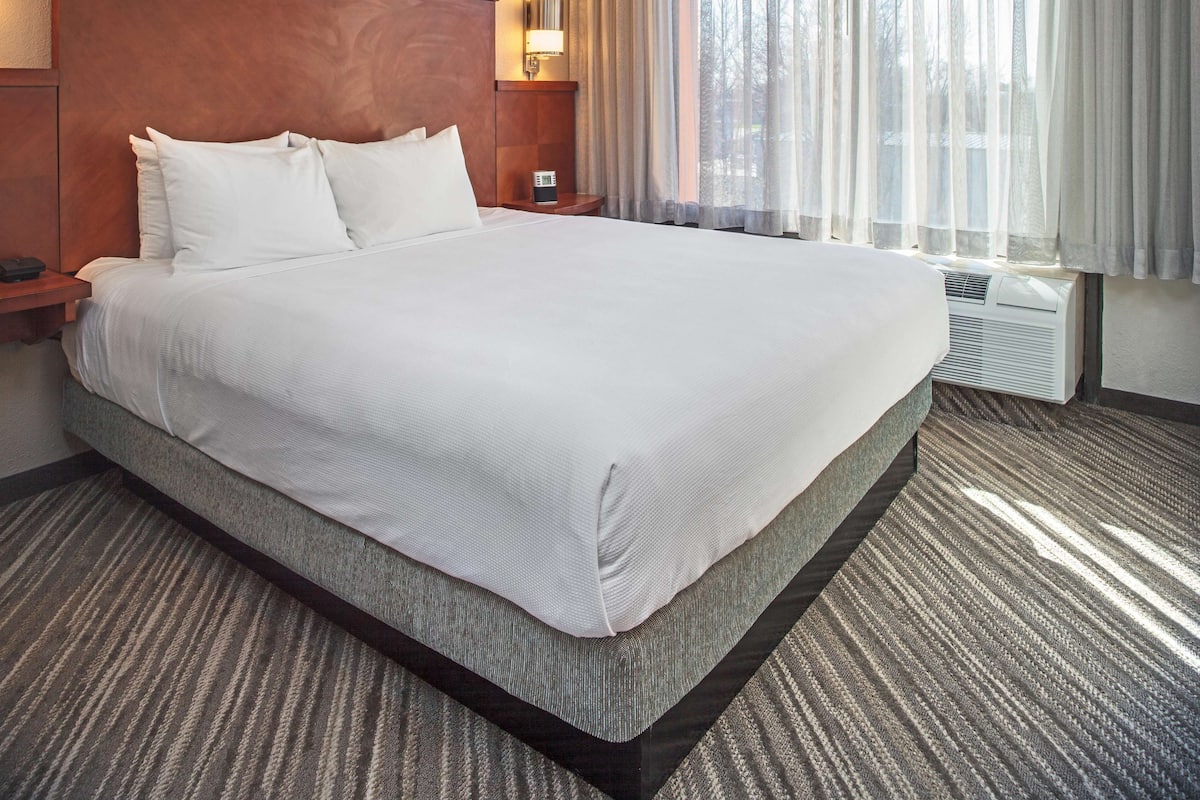A hotel room with a large bed, a nightstand, a lamp, and a window with curtains.
