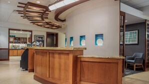 A reception area with a wooden reception desk, a modern ceiling design, and a view into the adjacent room. - Hyatt Place Cincinnati/Blue Ash (Cincinnati)