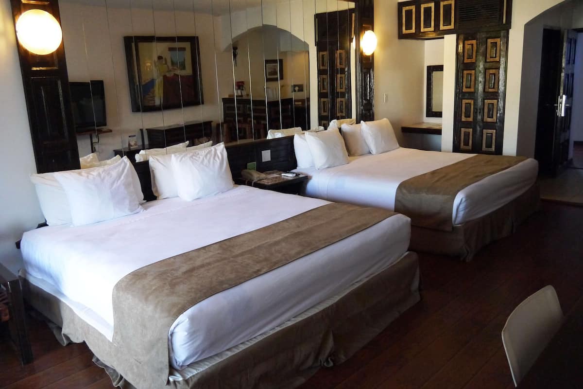 A hotel room with two beds, a television, a desk, and a mirror.