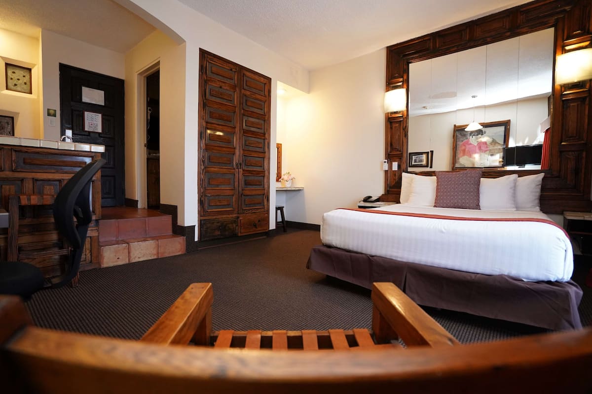 A hotel room with a bed, wooden desk, chair, and a large mirror.