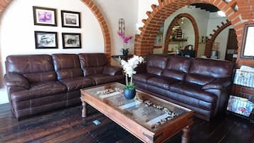 Una sala de estar con dos sofás de cuero marrón, una mesa de centro de vidrio con un centro de mesa floral y cuadros enmarcados en la pared.