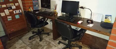 Un espacio de trabajo con dos sillas de oficina negras, un escritorio de madera, un monitor de computadora, un teclado, un ratón y una lámpara.