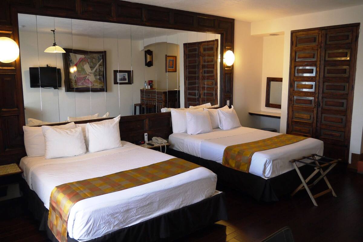 A hotel room with two beds, a large mirror, a television, and wooden wardrobes.