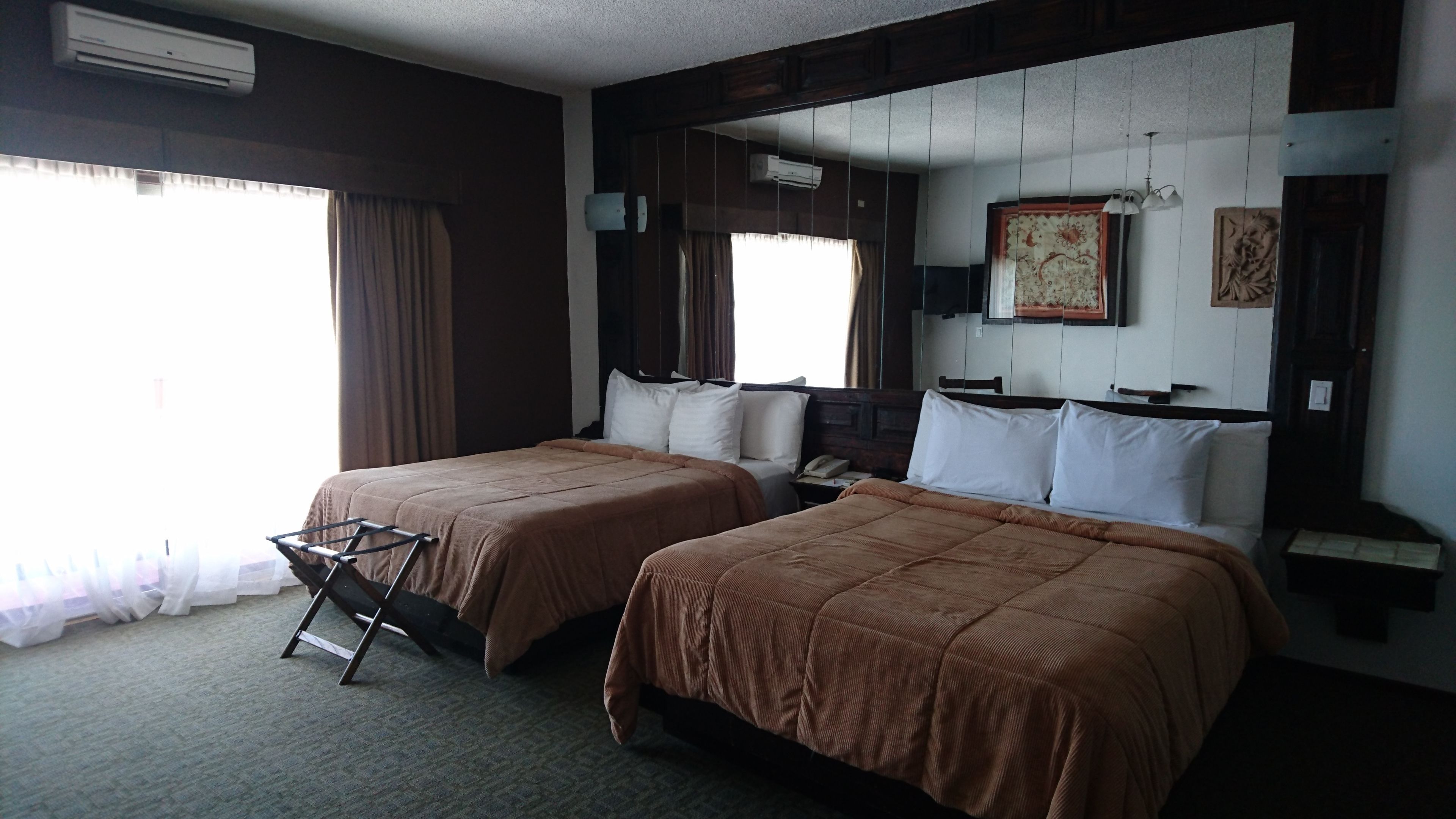A hotel room with two beds, a chair, a desk, and a window with curtains.