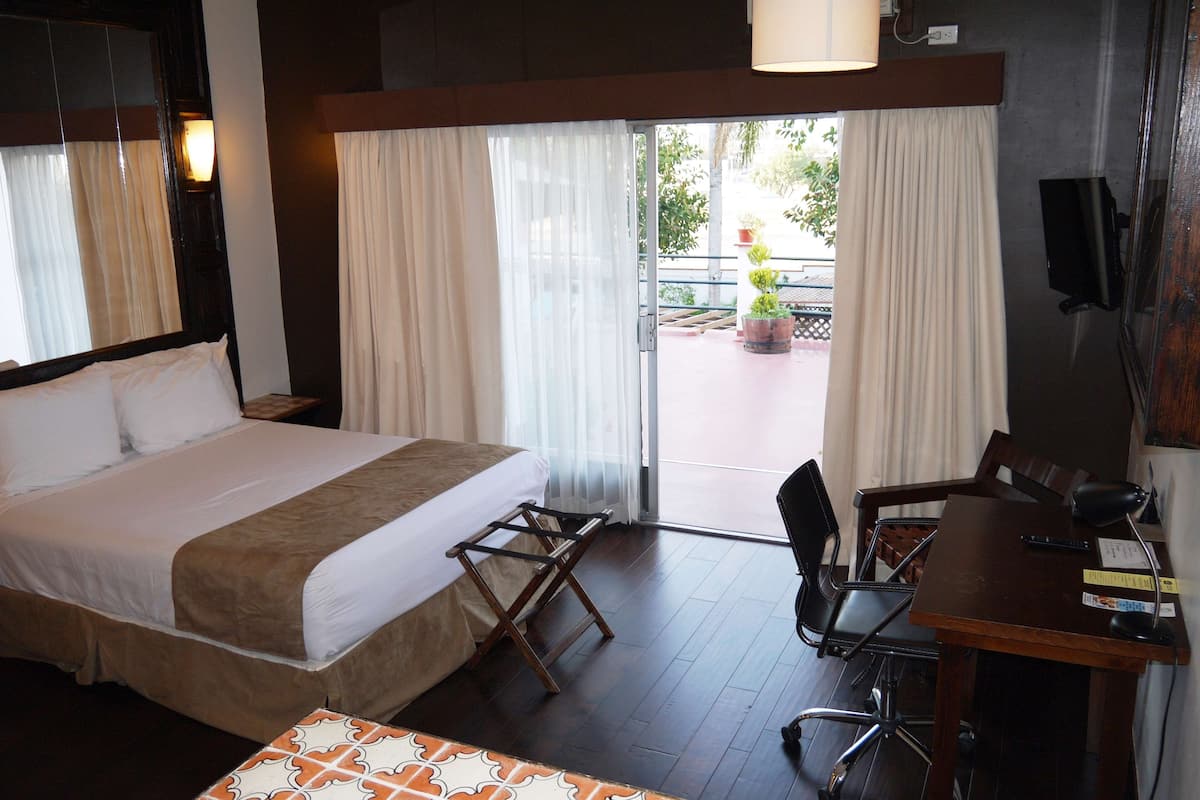A hotel room with a bed, a desk with a chair, a small table, and a view of the outside.