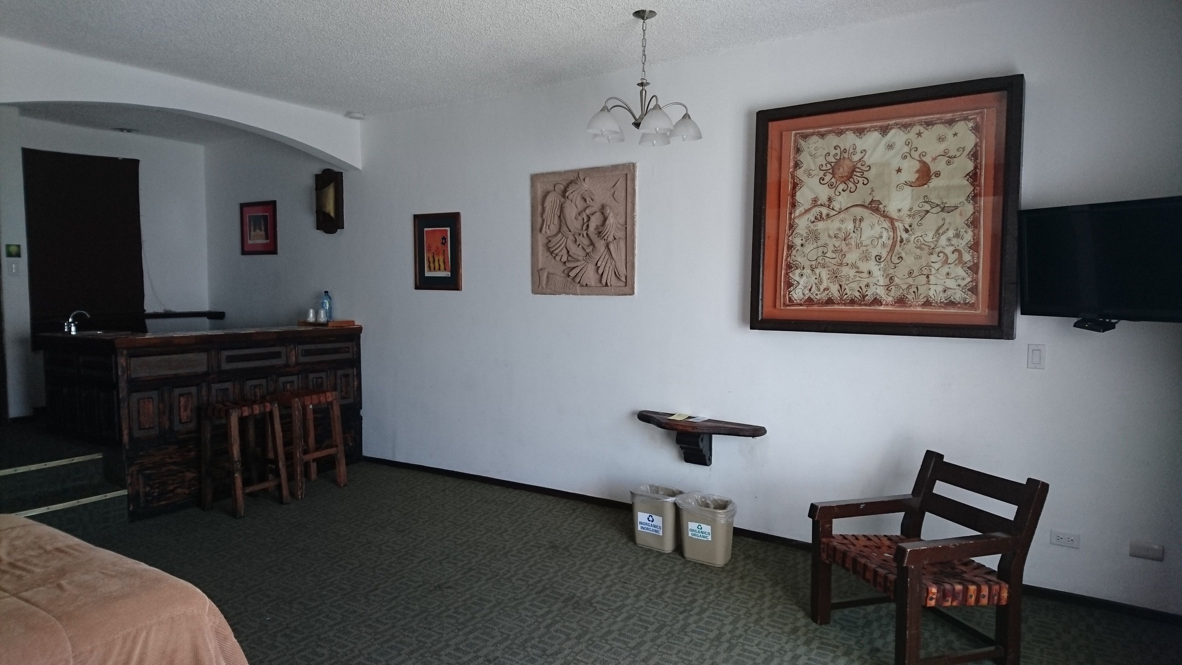 A room with a wooden bar, framed artwork, a chandelier, and a television on the wall.