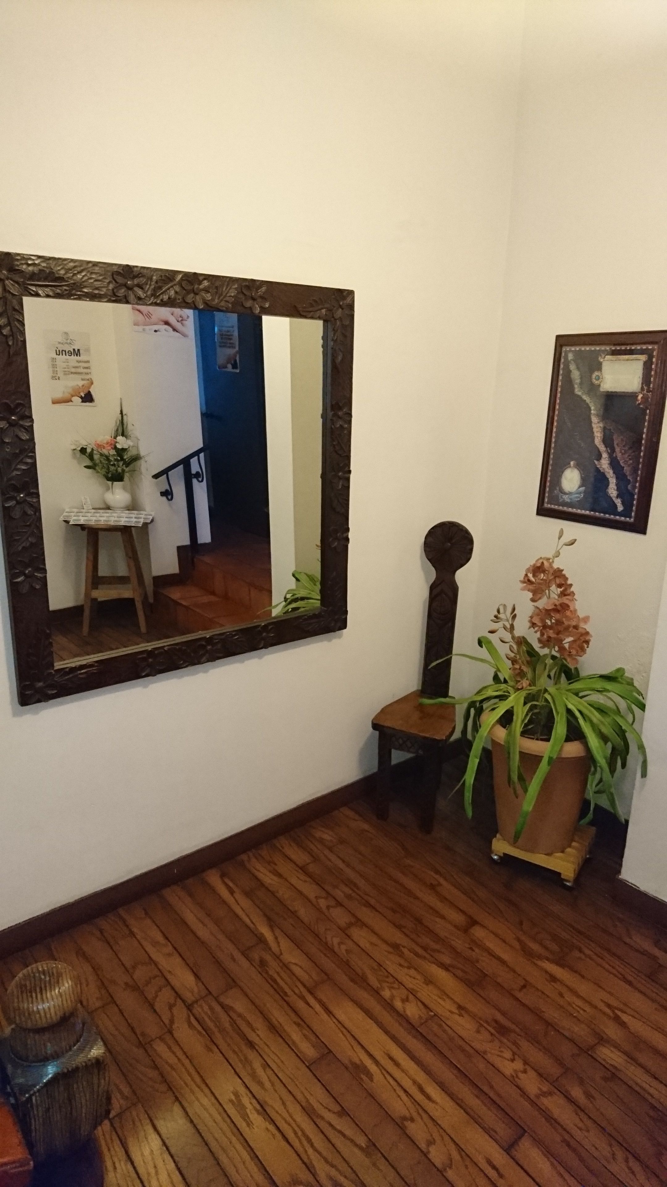 A room with a large mirror, a wooden stool, a potted plant, and a framed picture on the wall.