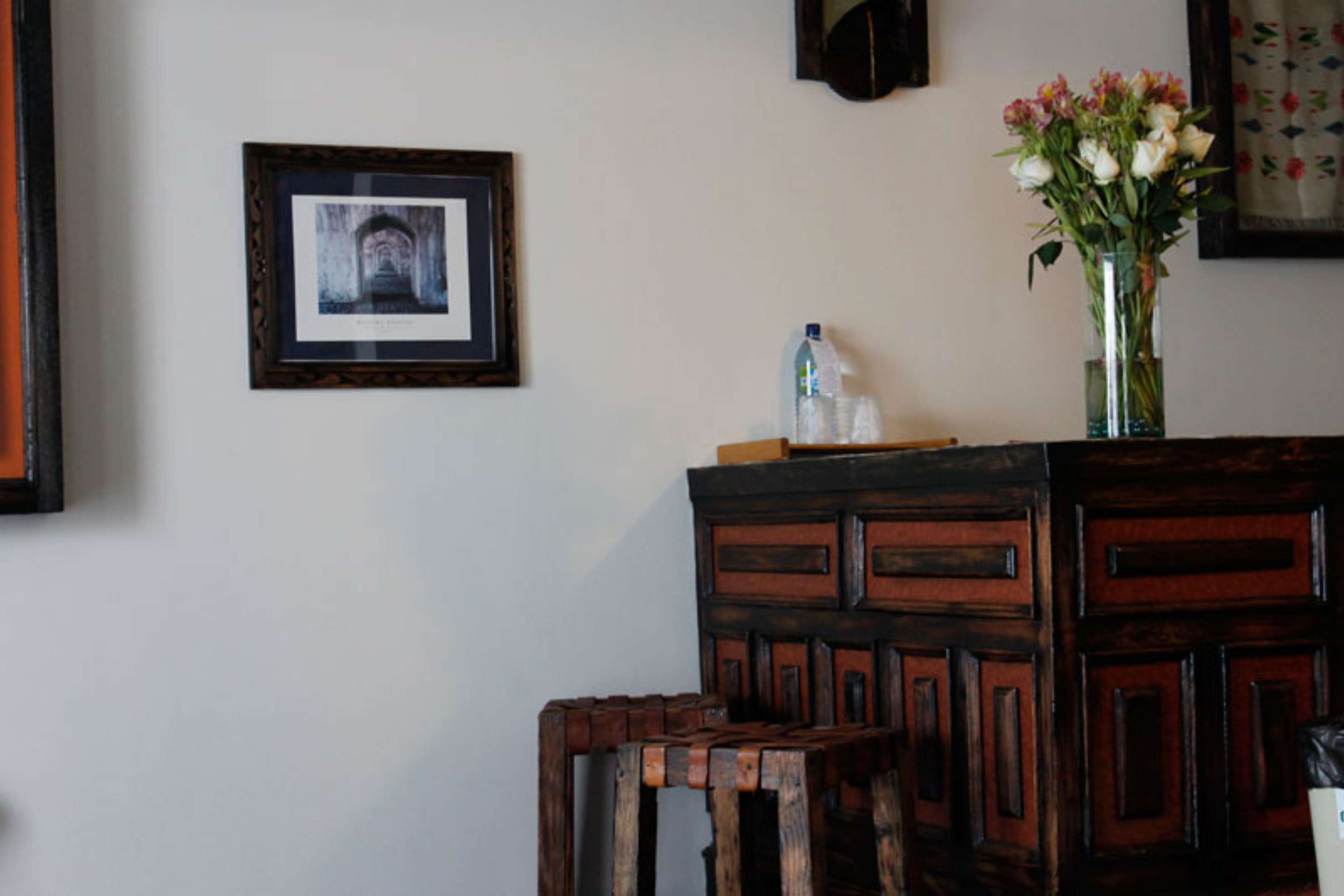 Un aparador de madera con un florero de flores, un cuadro en la pared y una botella sobre el aparador.