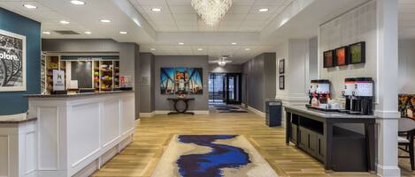 A hotel lobby with a reception desk, a coffee station, and a mural on the wall.