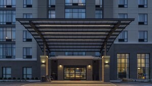 A modern hotel building with a prominent sign reading "Hampton Inn & Suites." It features a covered entrance with a glass canopy, multiple floors with large windows, and a brick facade. - Hampton Inn & Suites Newport/Cincinnati (Newport)
