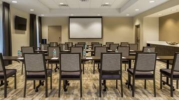 A conference room with a large screen, multiple tables, and chairs.