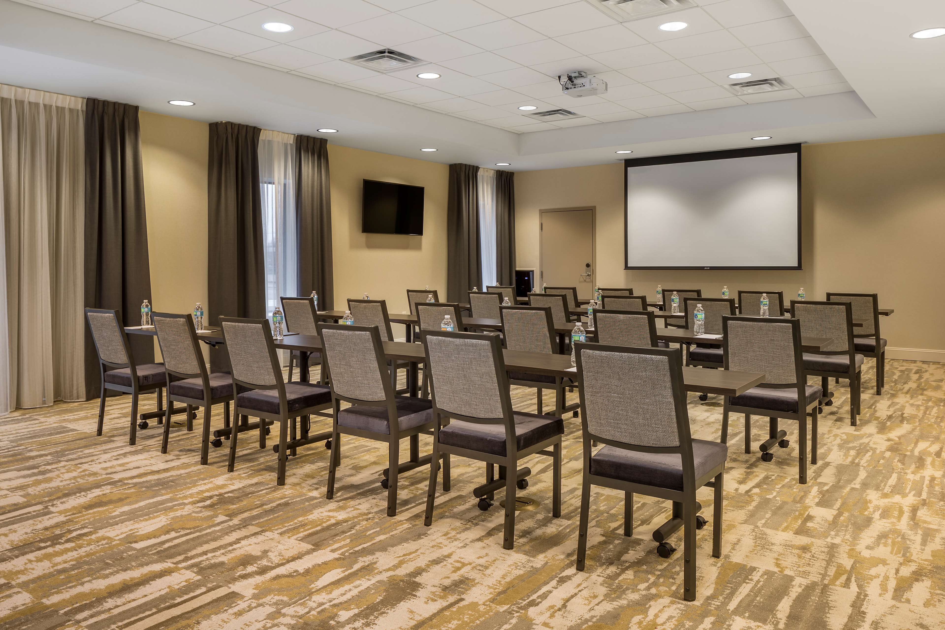 A conference room with rows of chairs, a projector screen, and a carpeted floor.