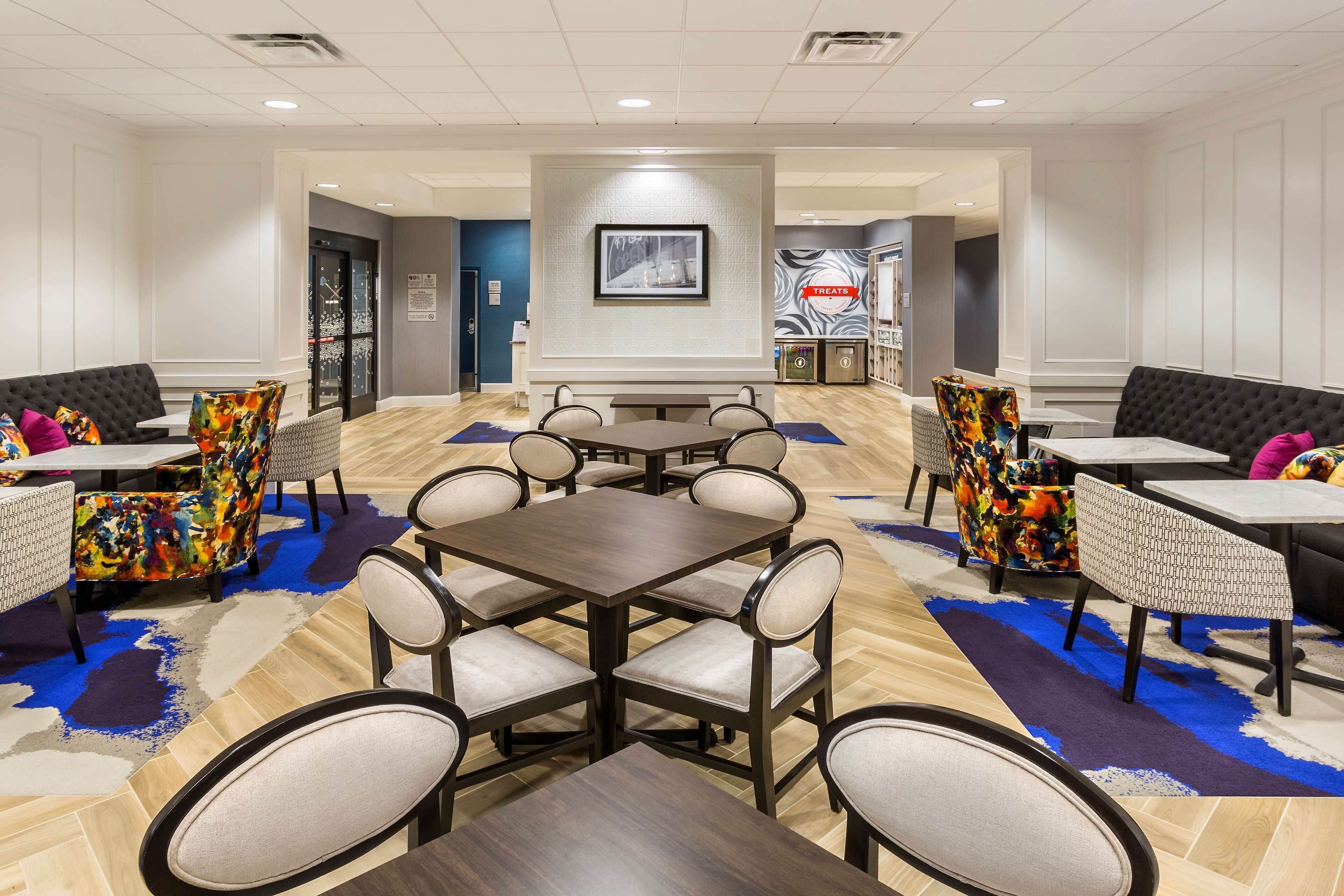 Un hall de hotel con zona de comedor central, diversas opciones de asientos y un mostrador de recepción.