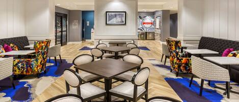 Un hall de hotel con zona de comedor central, diversas opciones de asientos y un mostrador de recepción.