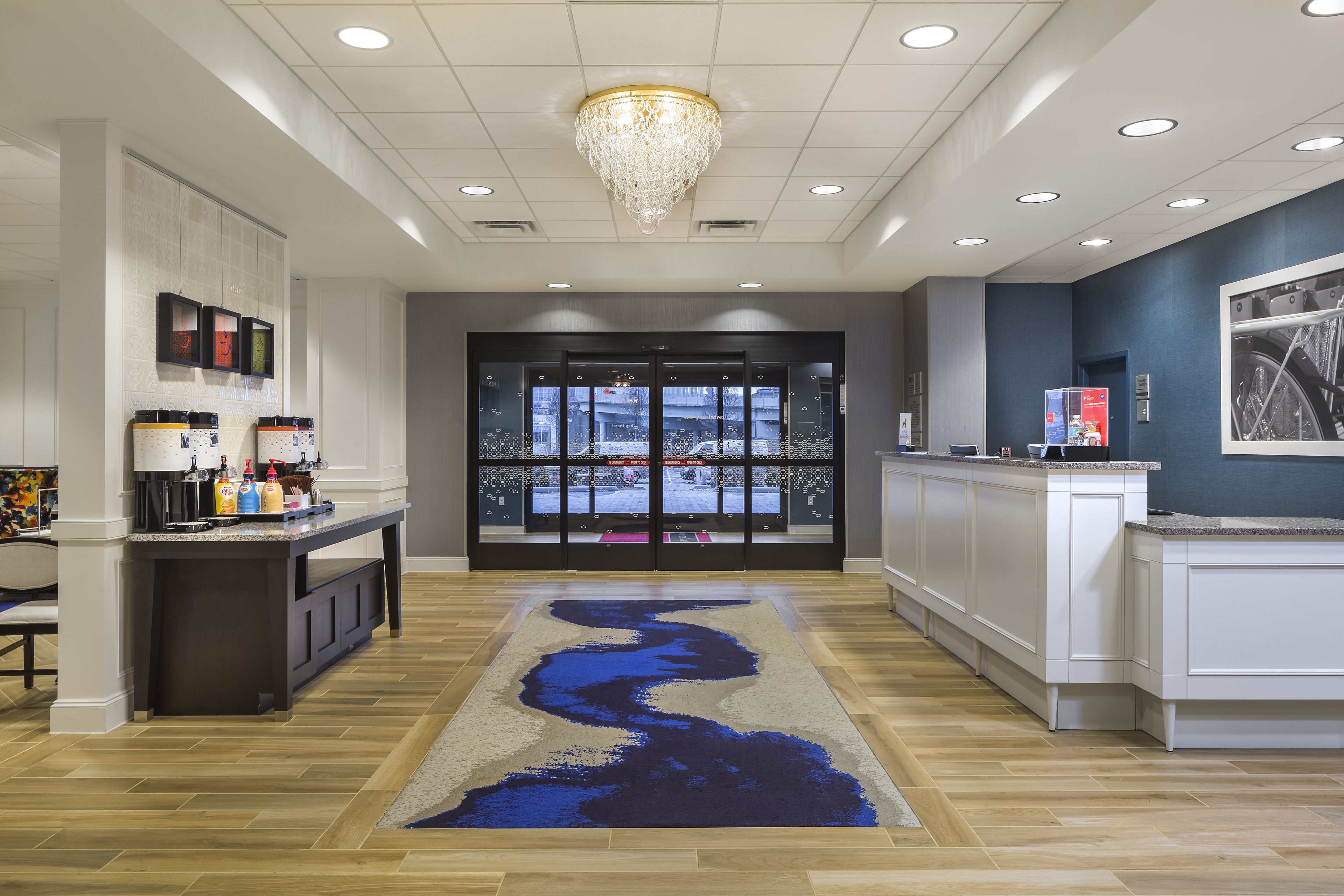 Un hall d’hôtel avec un comptoir d’accueil, un lustre, une grande fenêtre et un tapis bleu.