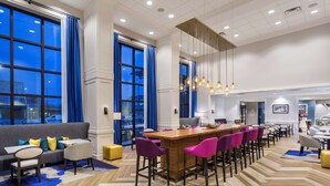 A spacious hotel lobby with a long bar, comfortable seating, and large windows offering city views. - Hampton Inn & Suites Newport/Cincinnati (Newport)