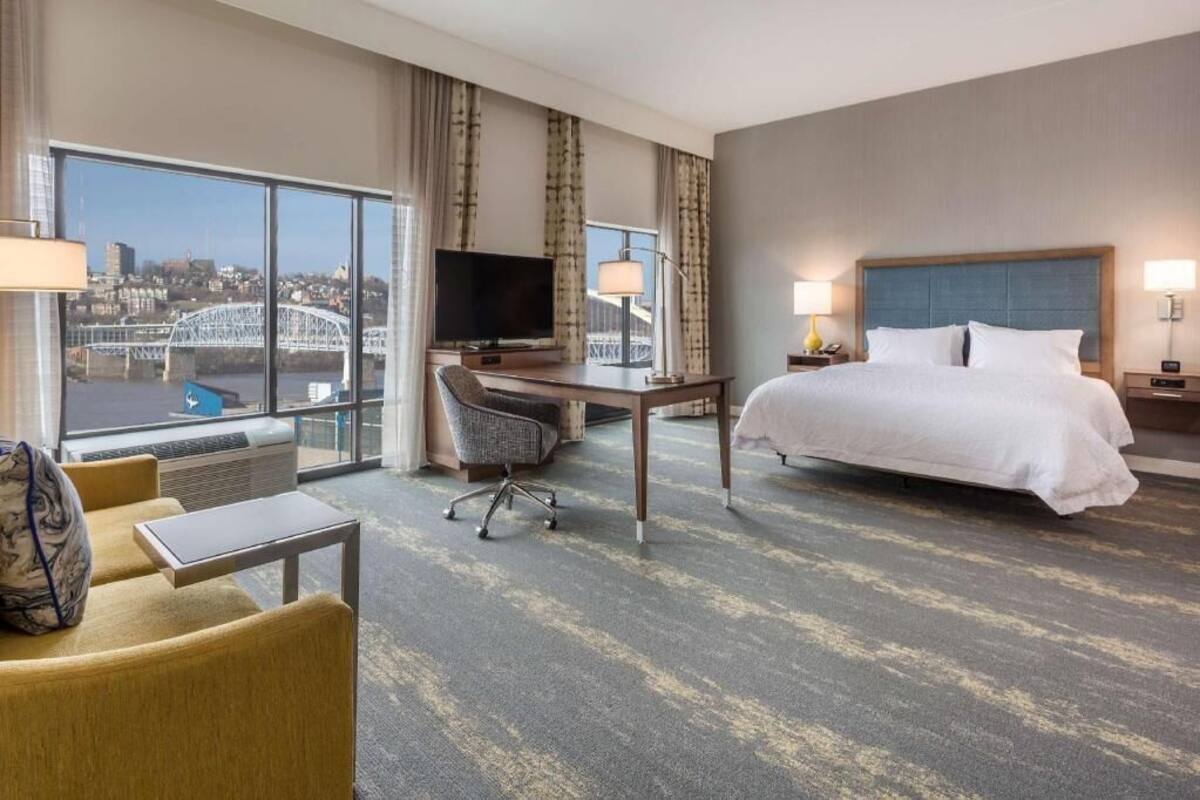 A hotel room with a bed, desk, TV, and a view of a bridge.