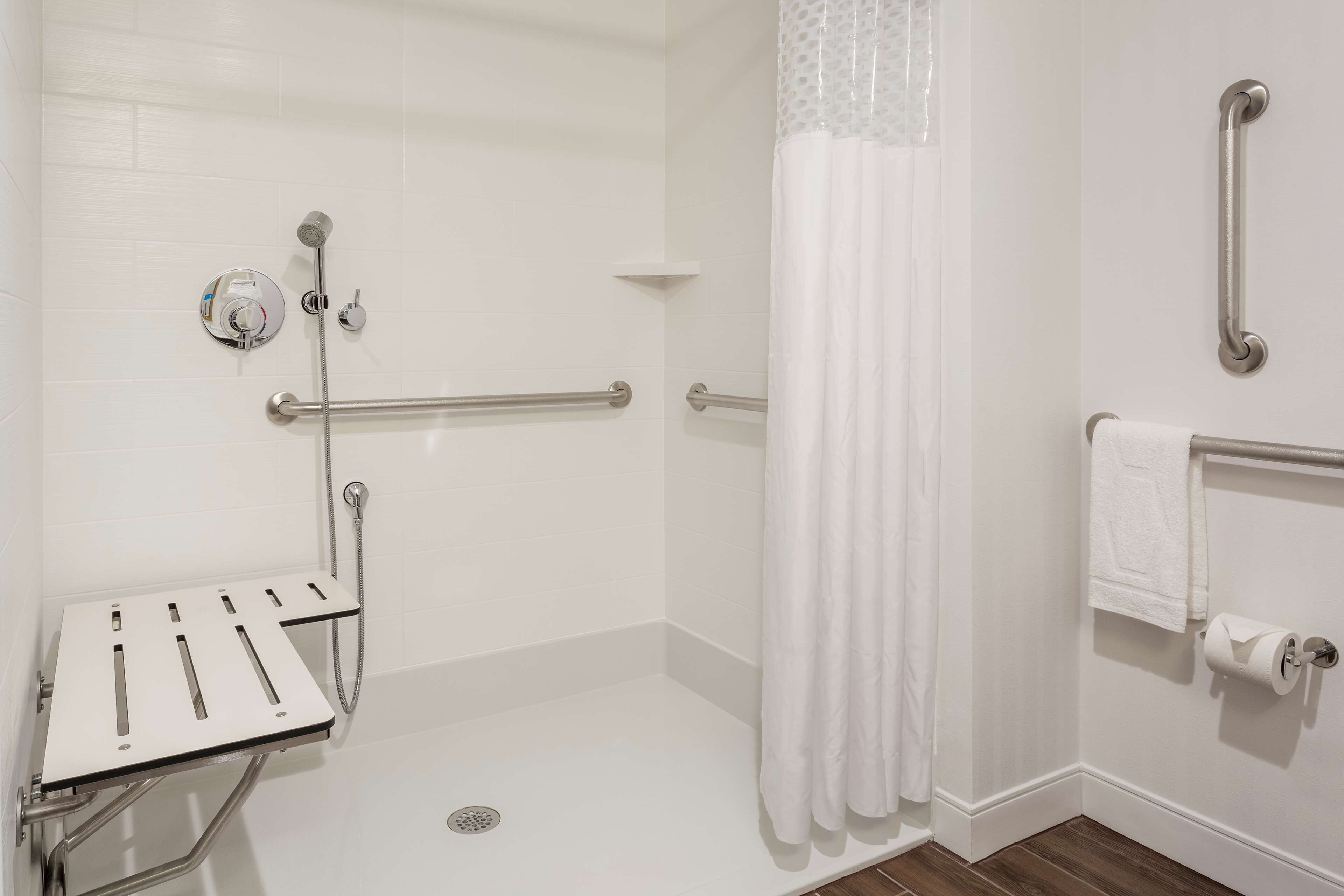 A wheelchair-accessible shower area with grab bars, a shower control panel, and a white shower curtain.