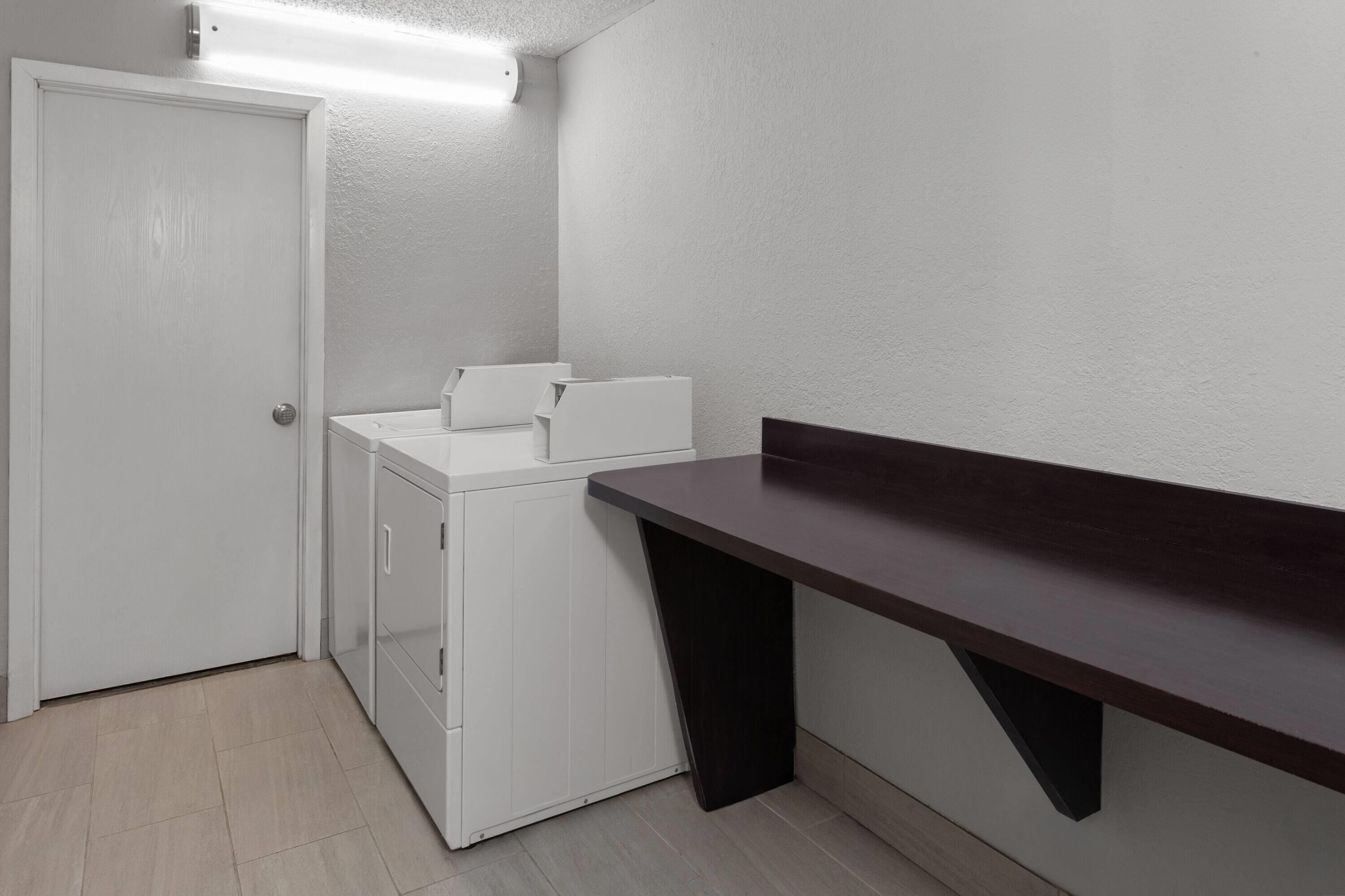 Un lavadero con una lavadora blanca, un tendedero y un banco de madera oscura.